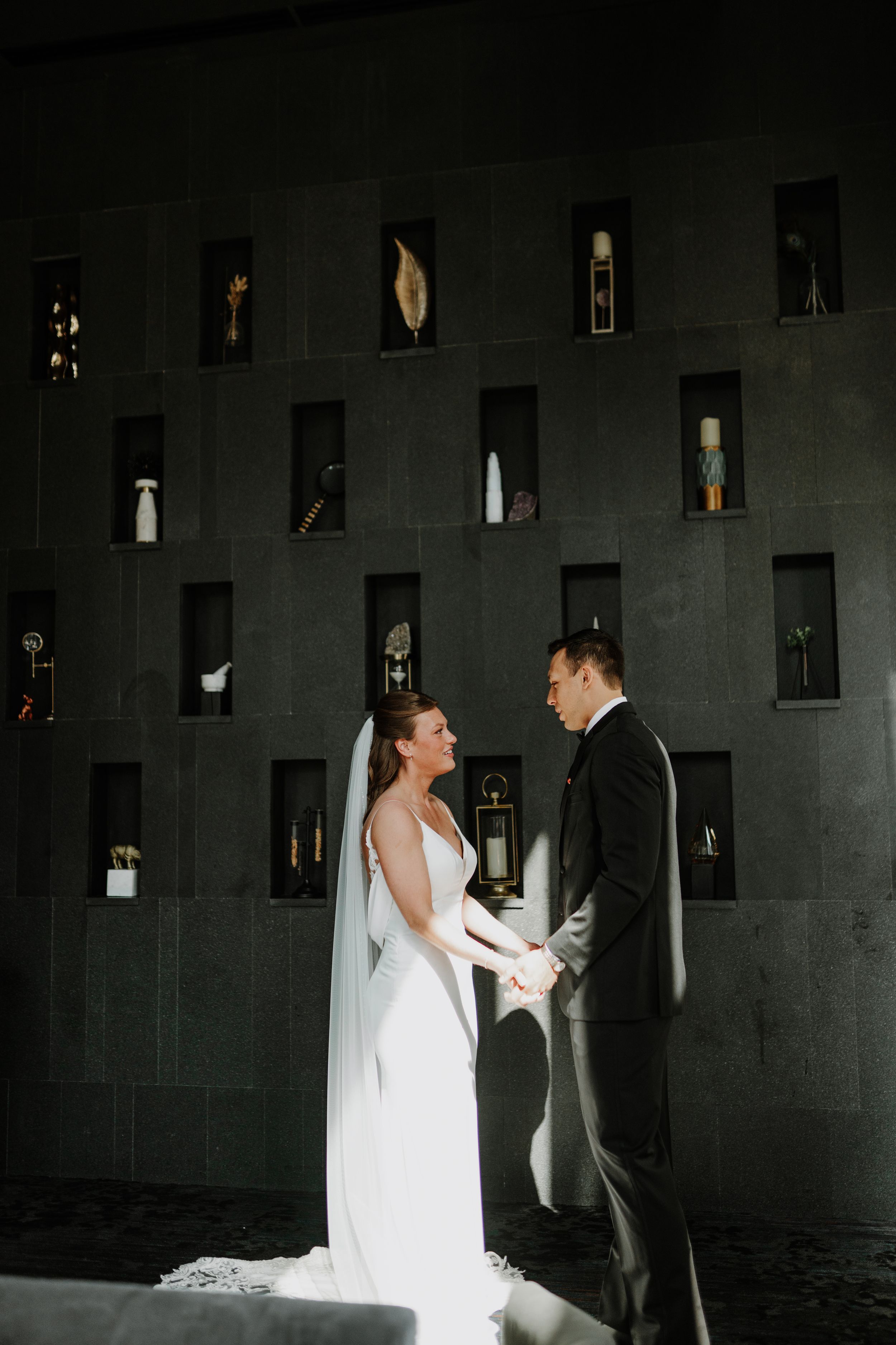Intimate wedding couple moment in dramatic lighting against dark wall with wine bottle display.