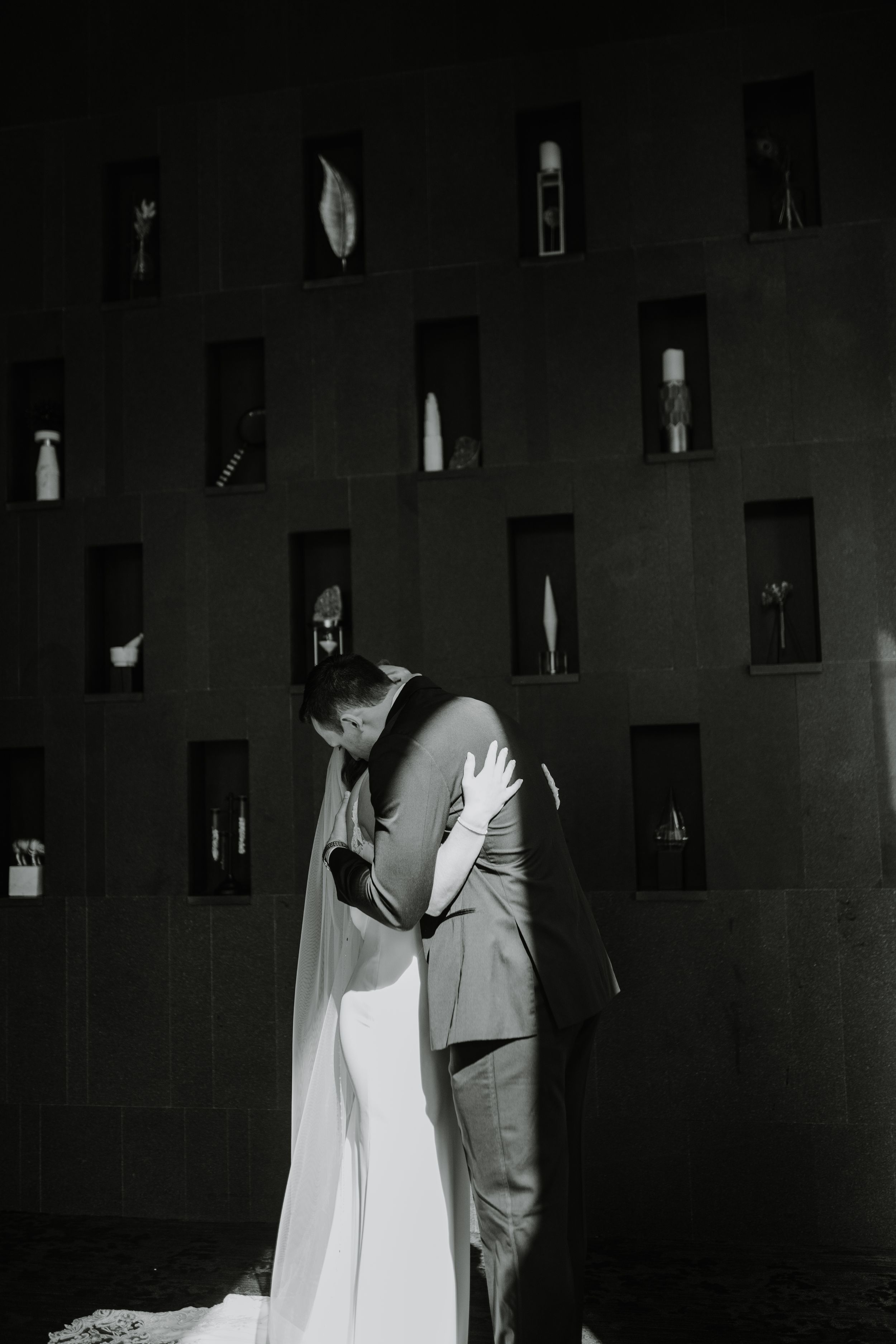 A couple shares an intimate moment in front of a decorative wall with small display niches at their wedding.