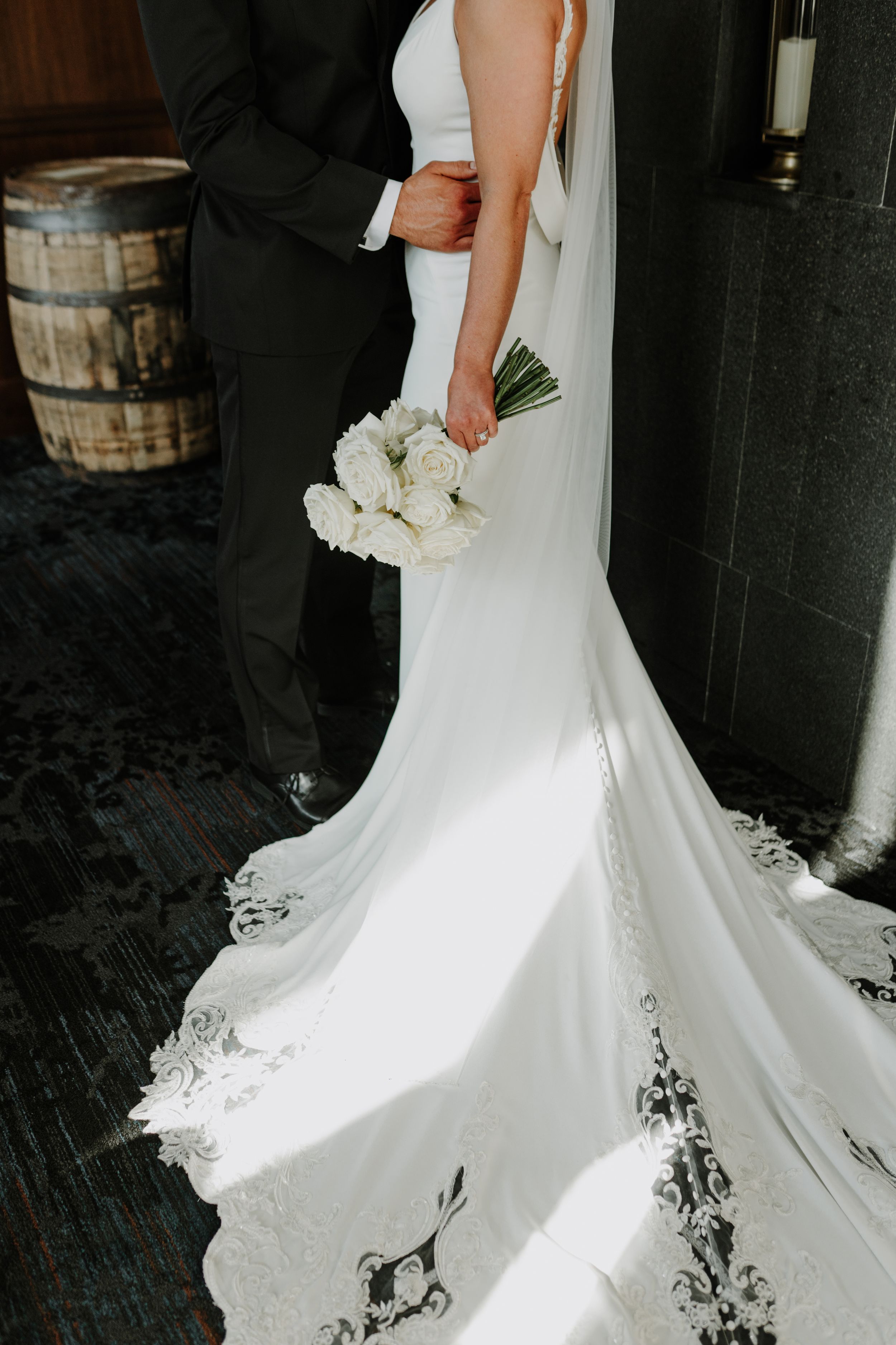 Detail shot of bride's flowing white wedding dress train and bouquet against dark background.