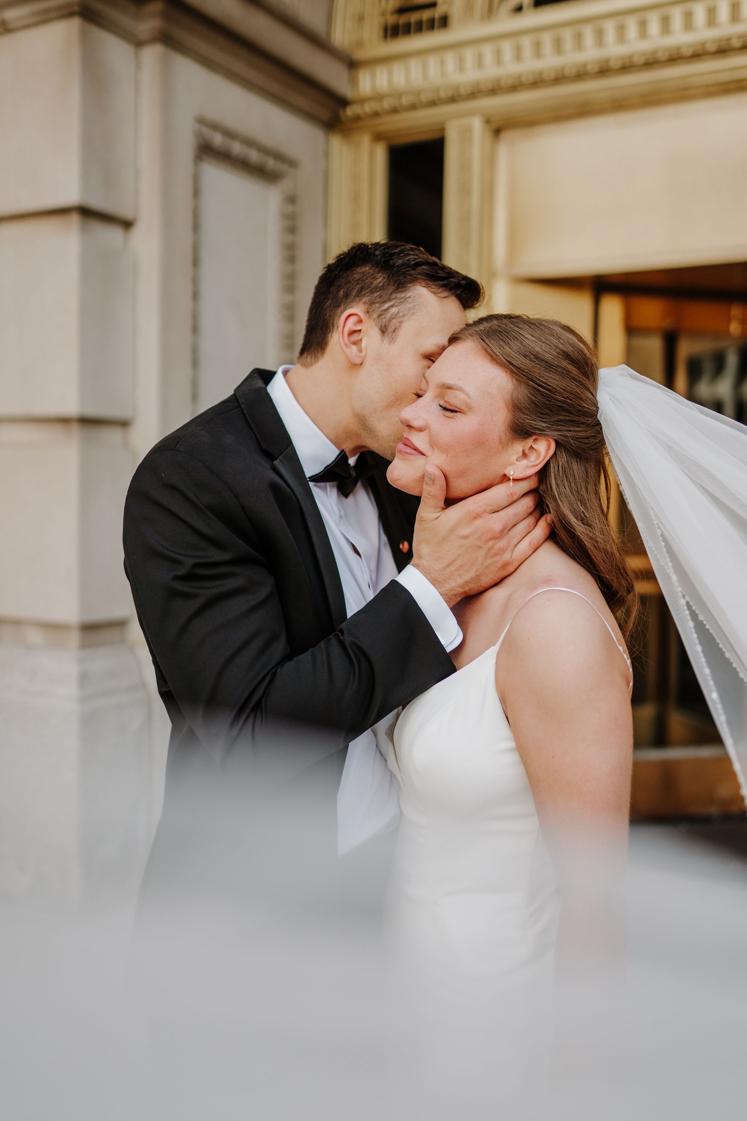 Closeup of tender moment between newlyweds outside elegant building.