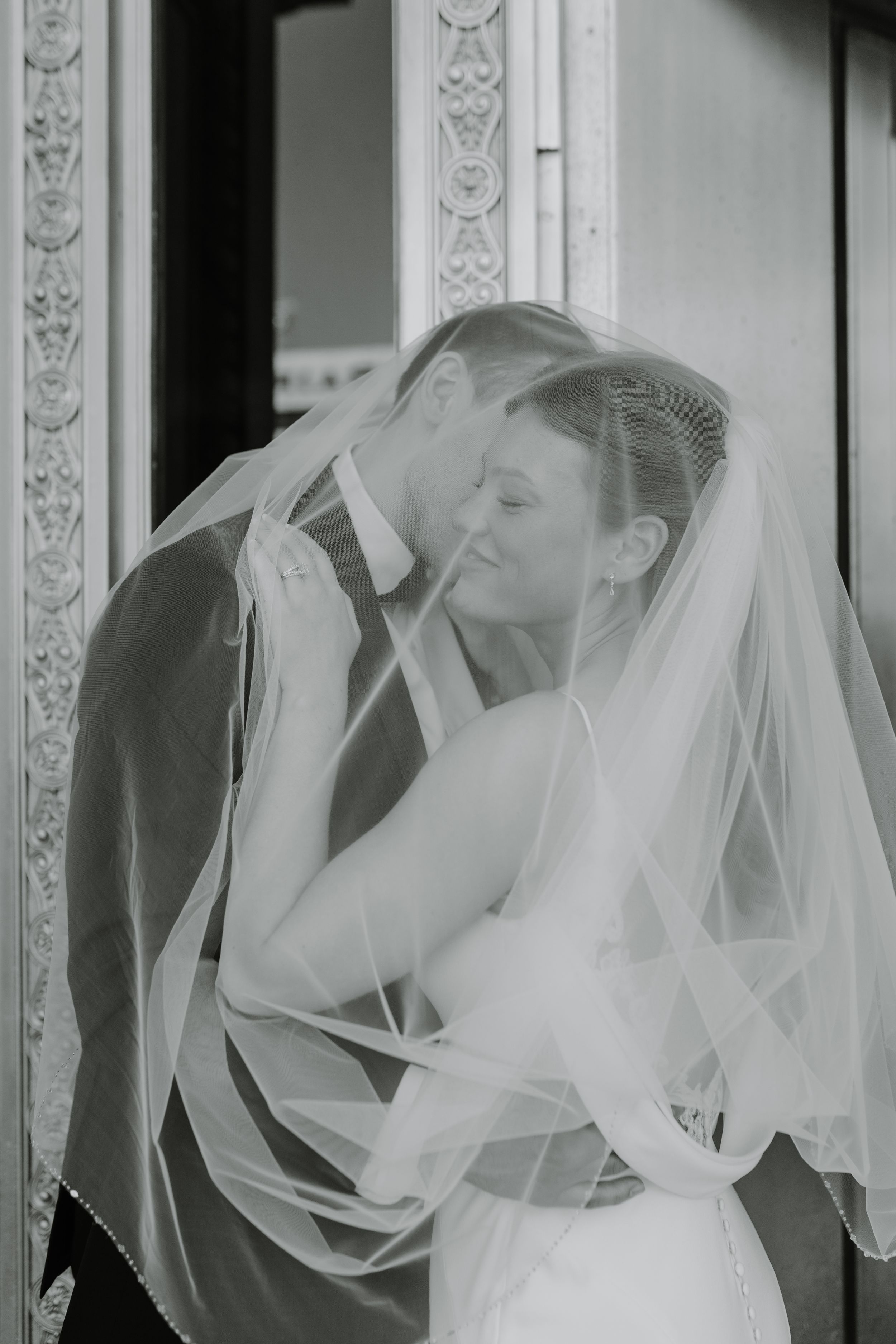 Black and white portrait of couple sharing intimate moment through bride's delicate veil.