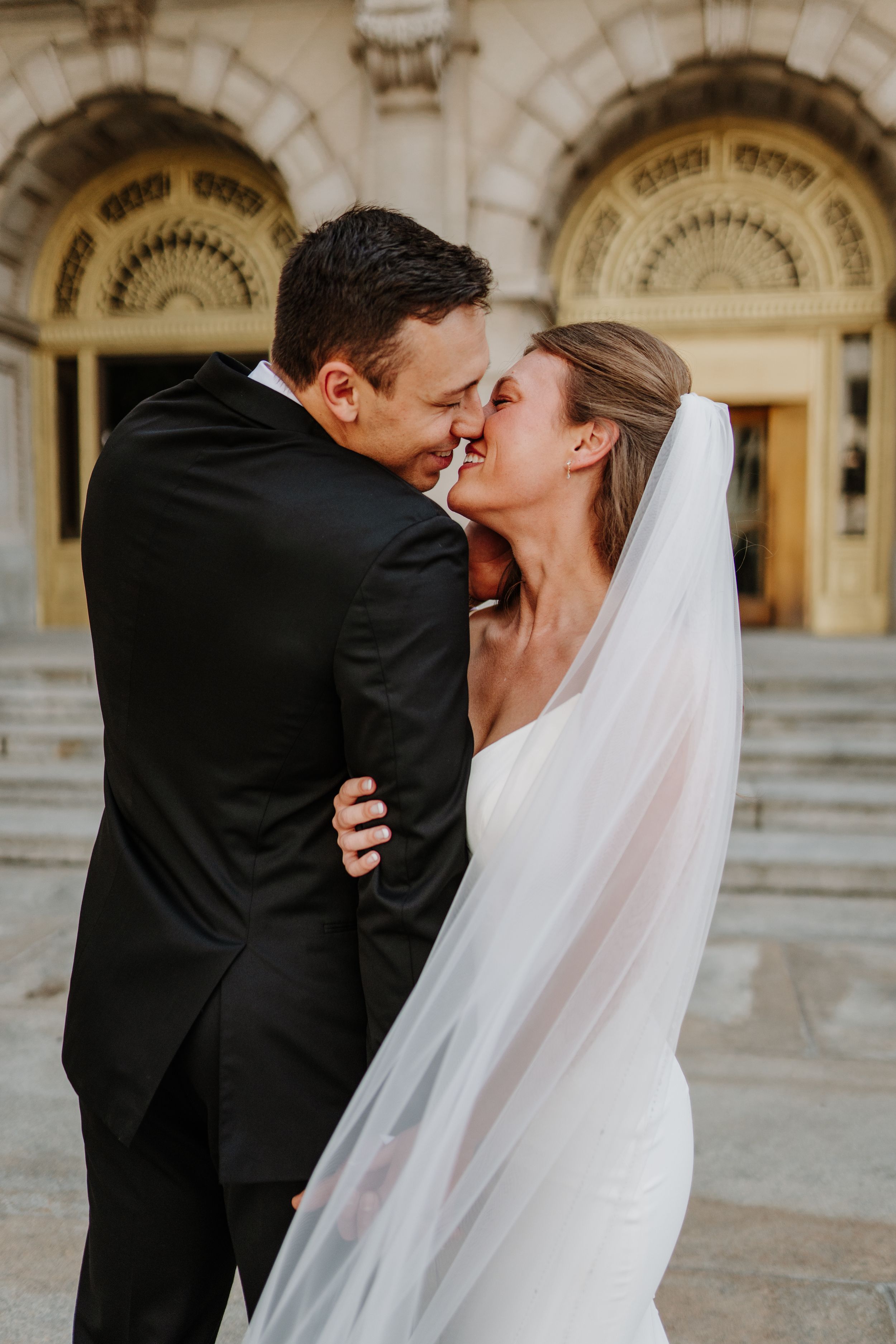 Romantic newlywed couple sharing intimate kiss beneath ornate archway.
