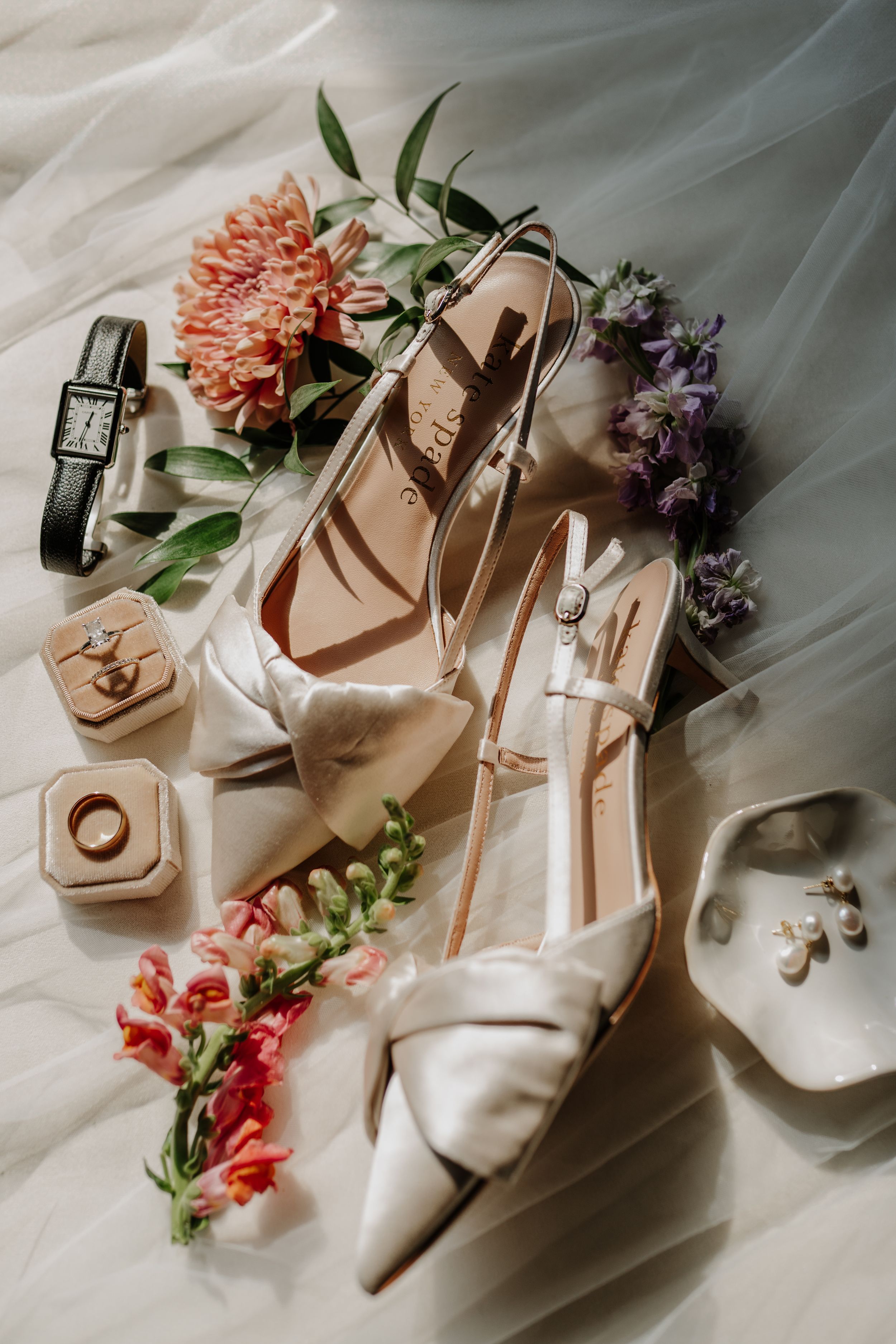 Bridal accessories including white heels, flowers, and jewelry arranged on white fabric.