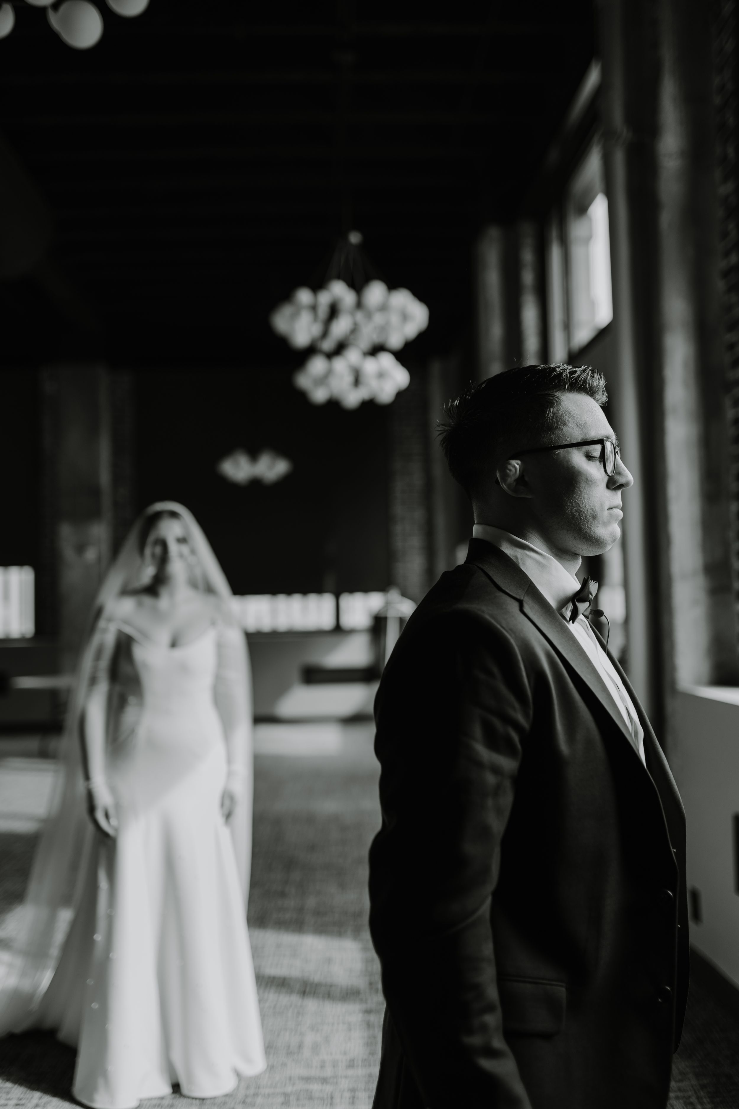 Artistic black and white portrait of wedding couple standing in dramatic window light.
