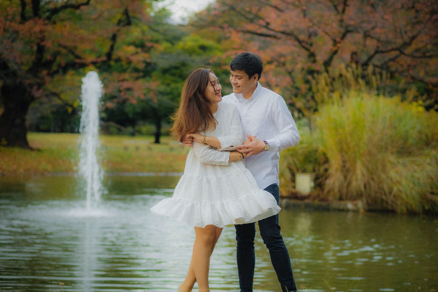 A romantic couple embraces near a fountain in an autumn park setting.