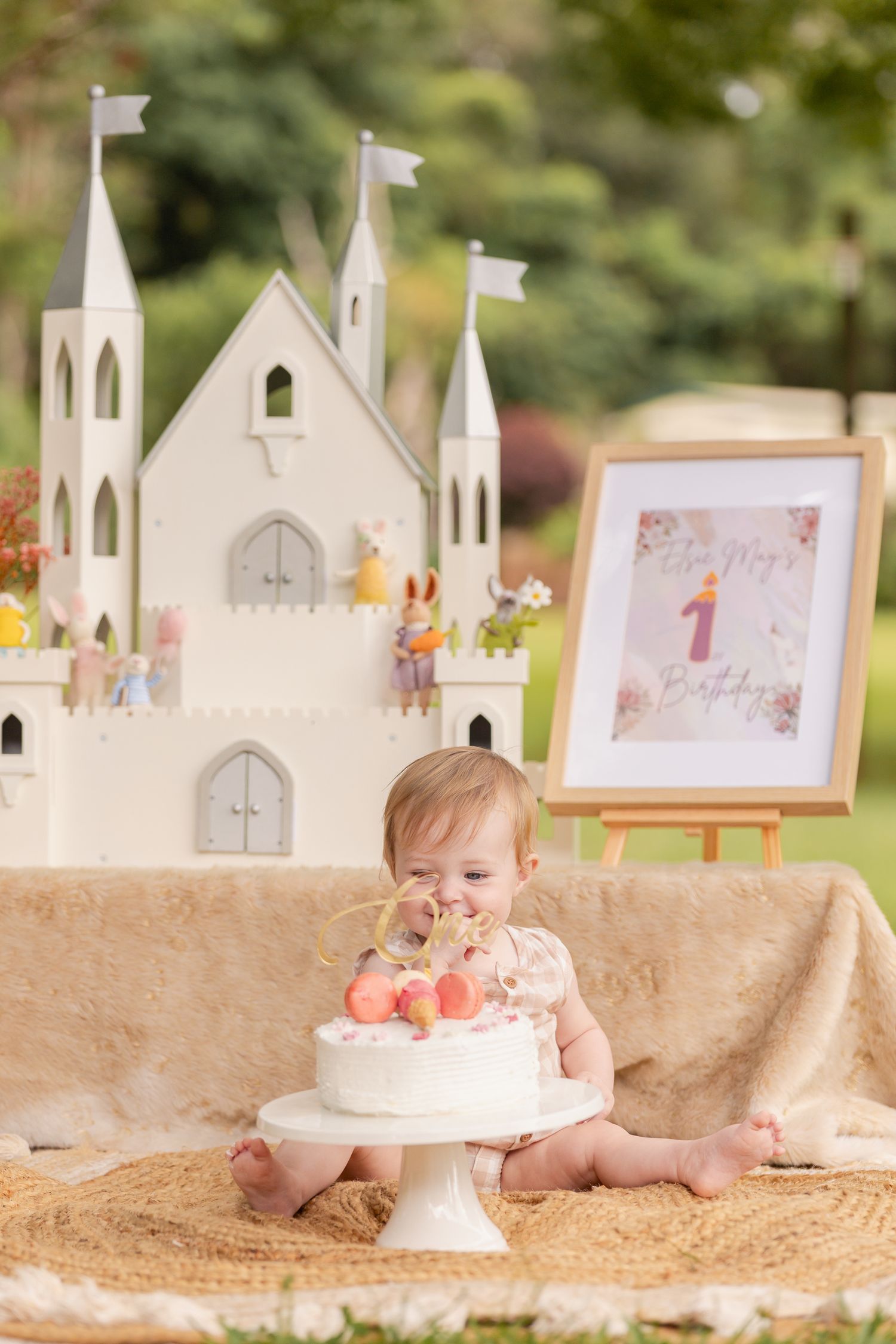 First birthday setup with white paper castles, cake, and decorations on burlap backdrop.