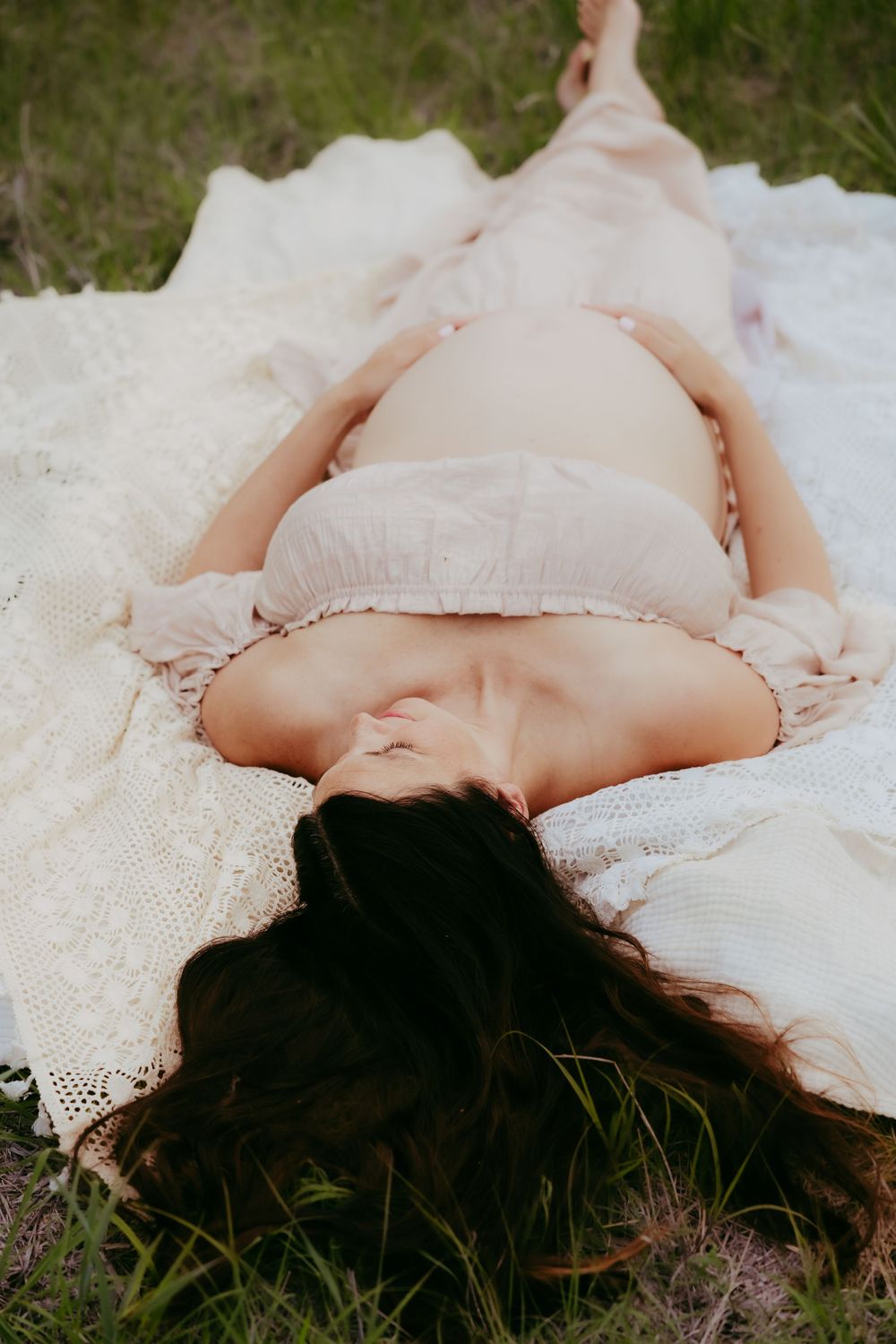 A person lying on the grass in a delicate white lace dress creating a dreamy ethereal outdoor portrait.