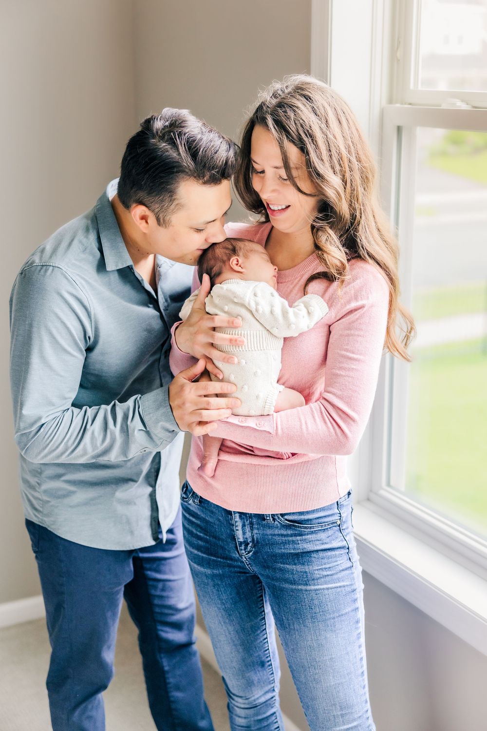 Couple in blue denim and pink sweater share tender moments by a bright window in four connected photographs.