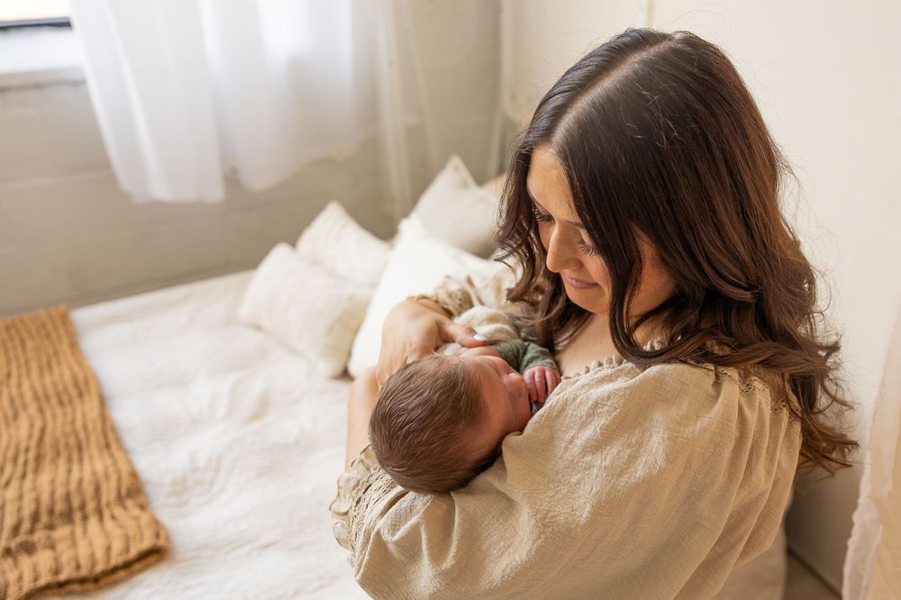 A tender moment between parent and newborn baby in a cozy bedroom setting.