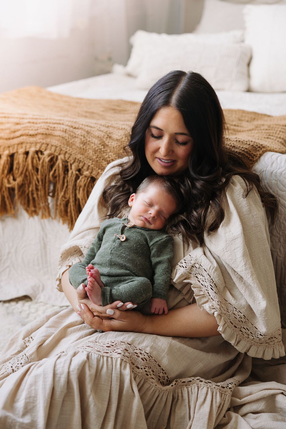 Parent cuddles with newborn baby wearing green on a bed with white and beige linens.