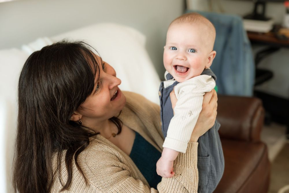 Joyful interaction between mother and baby filled with laughter in bright living room.