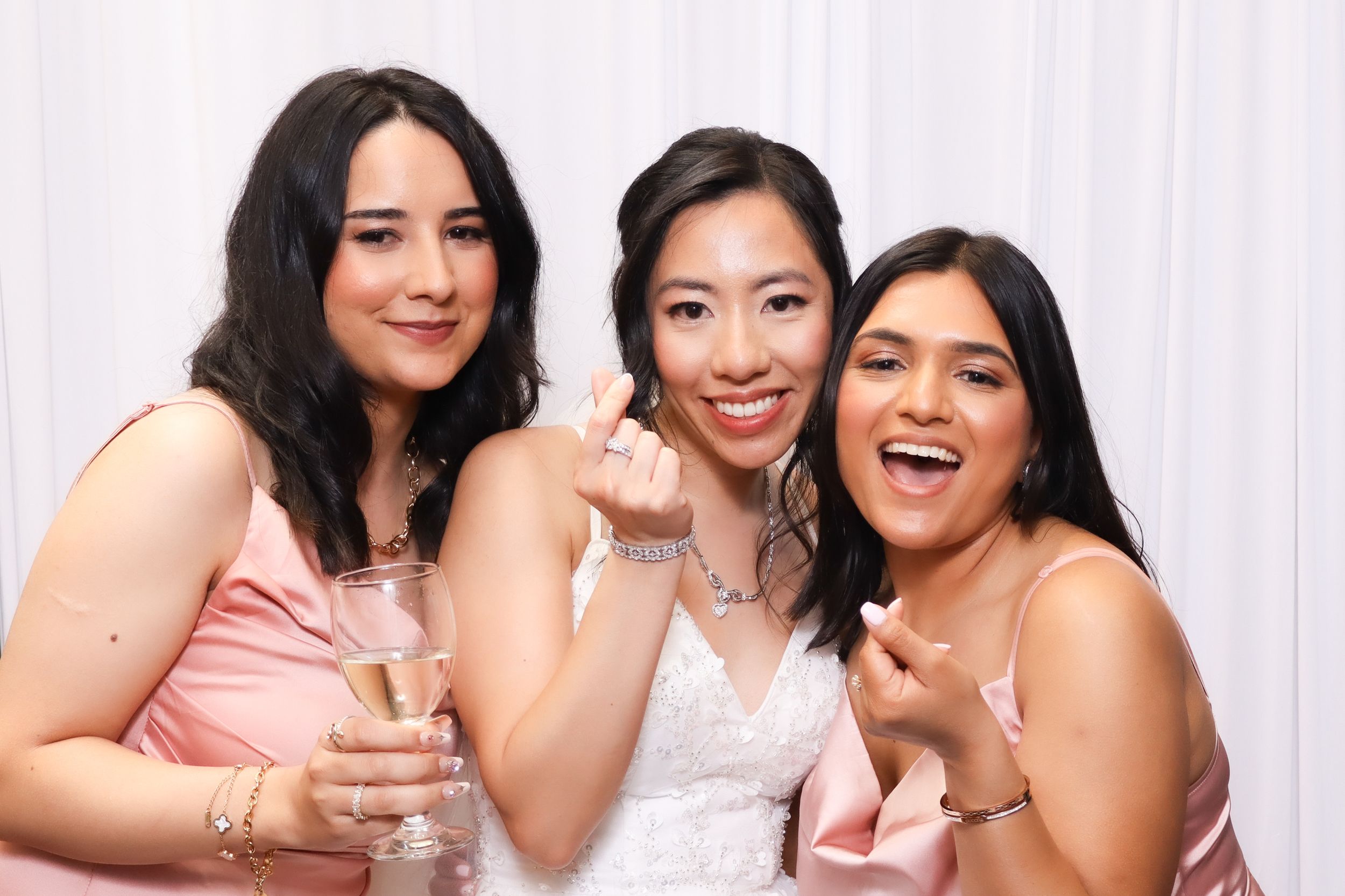 Three friends in formal attire pose together with drinks at a celebration.