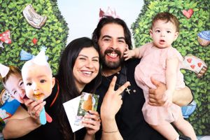 Happy family poses against a decorative green hedge wall with floating butterflies and floral accents.