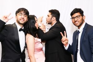 Group in formal attire at a party making peace signs against white backdrop.