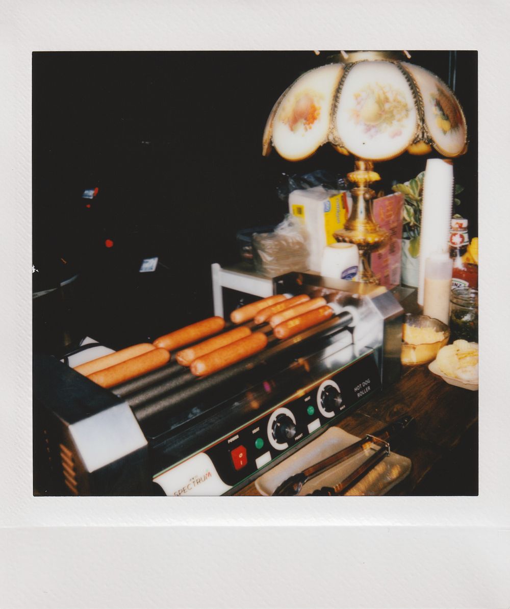 Vintage hot dog roller grill machine under retro amber glass lampshade in dim lighting.