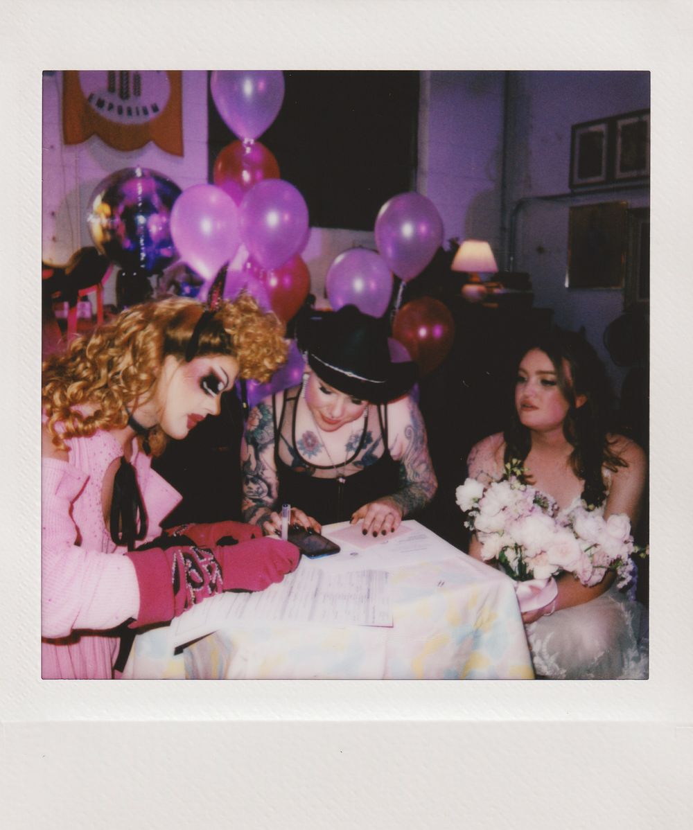 Party scene with purple and pink balloons and people gathered around a table.
