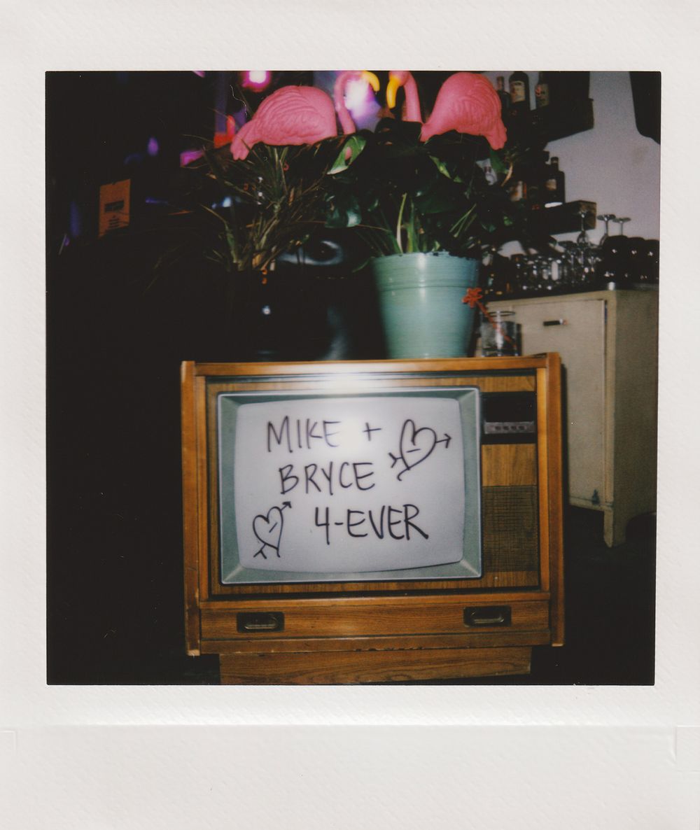 Handwritten 'Mike + Bryce 4-ever' note with hearts displayed on vintage TV with plant on top.