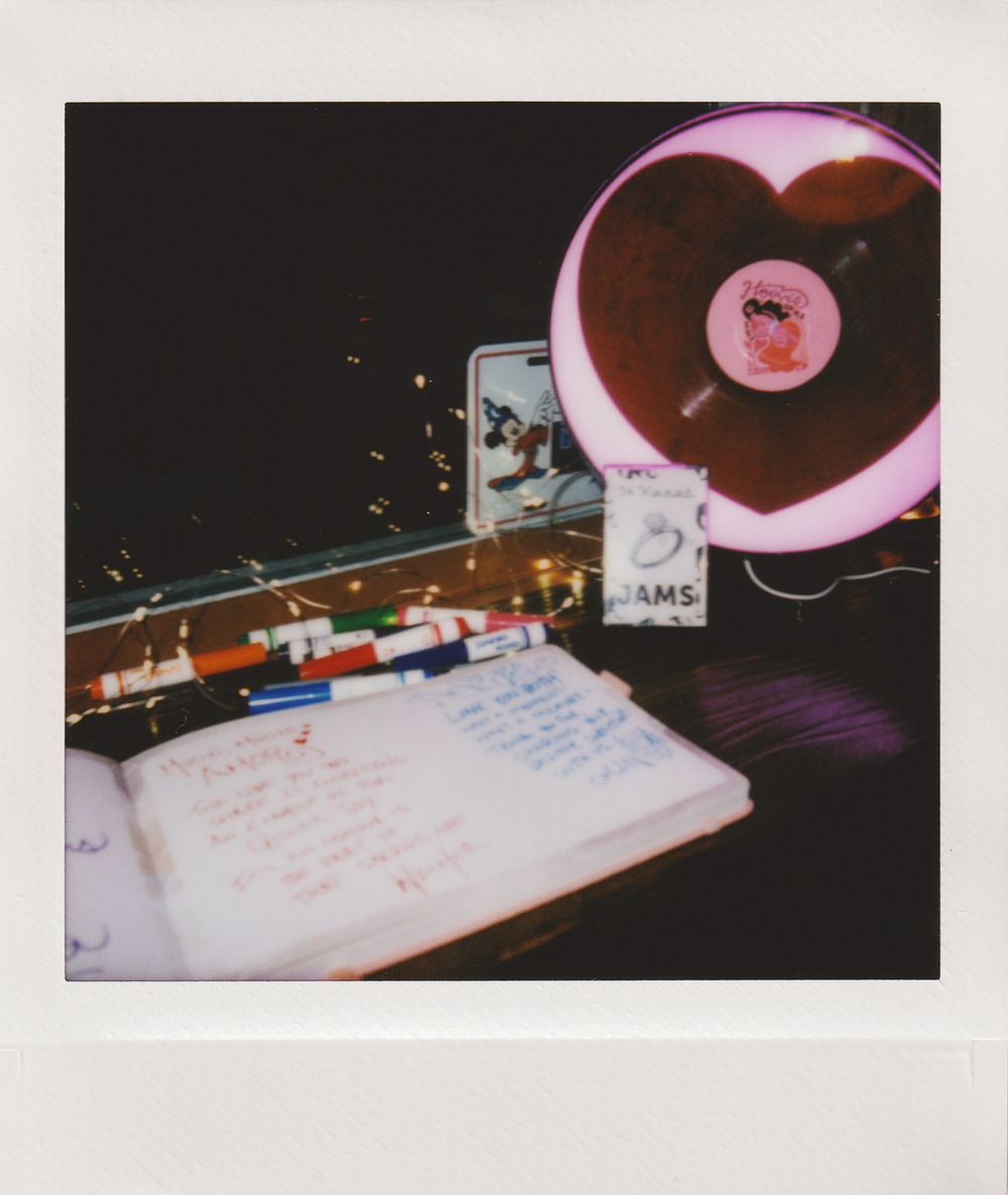 Record player and notebook with handwriting under pink lighting in a dark room.
