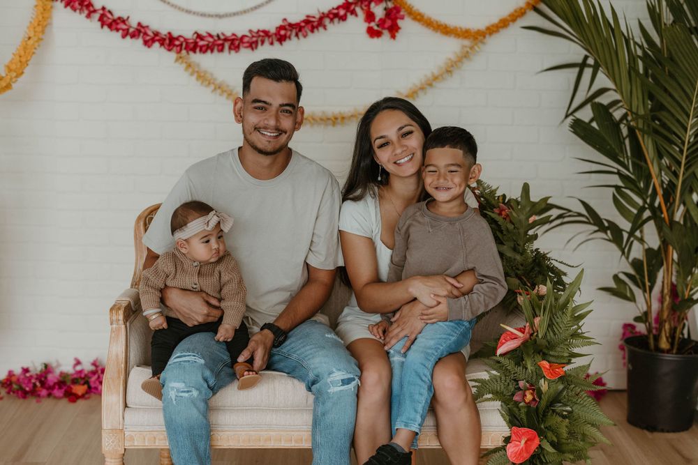 A family sitting together on a white bench with festive garlands and plants in the background.