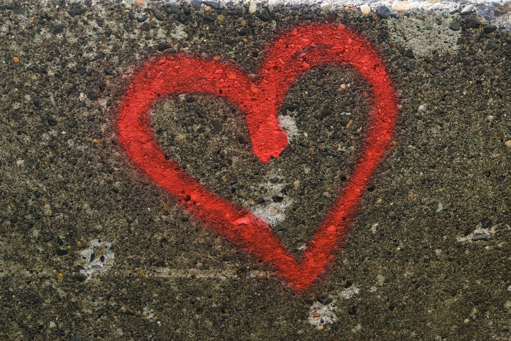 Red heart graffiti spray painted on weathered concrete wall.