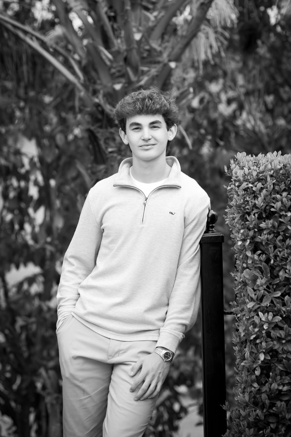 Black and white portrait series taken outdoors with decorative shrubs and natural lighting.
