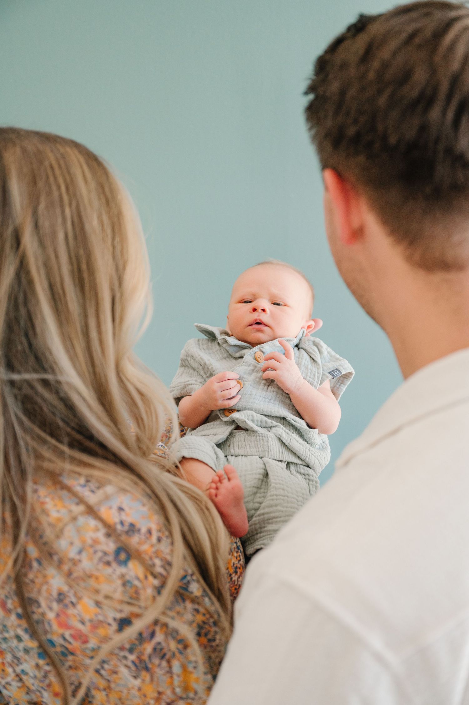 Parents holding their newborn baby against a blue wall background.