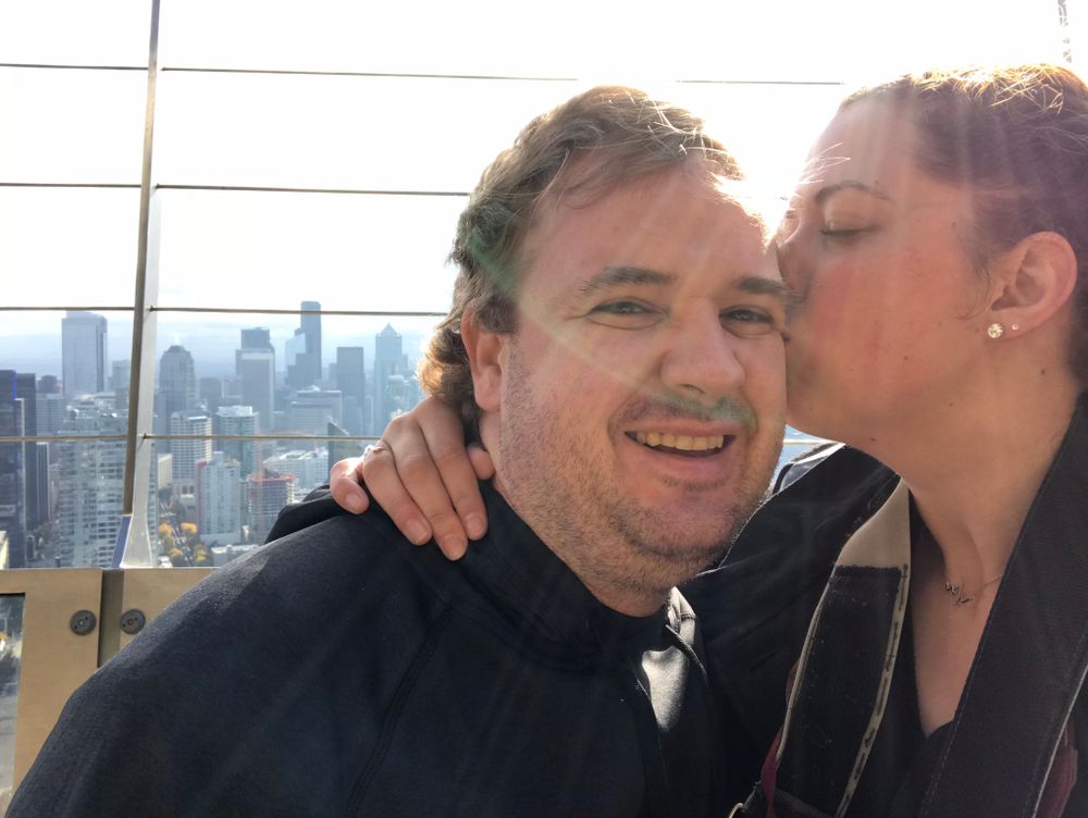 A couple sharing an affectionate moment on an observation deck overlooking a city skyline.