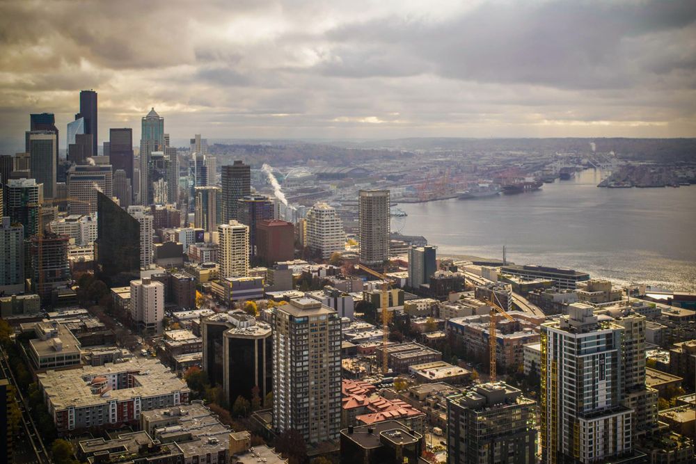 Dramatic aerial view of Seattle's downtown skyline and waterfront under cloudy skies.