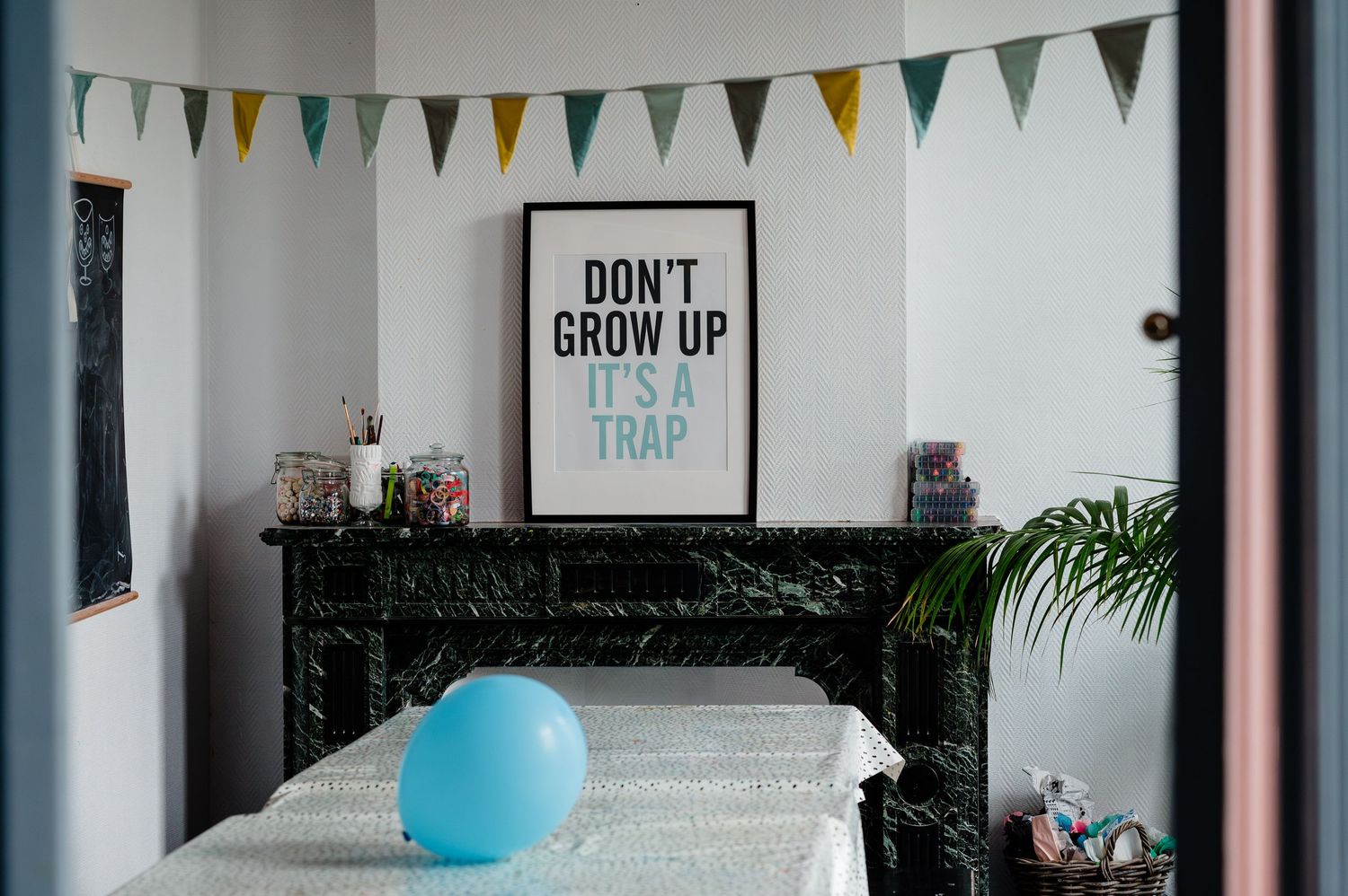 A modern room decorated with bunting flags and a "Don't Grow Up" poster above a marble fireplace.
