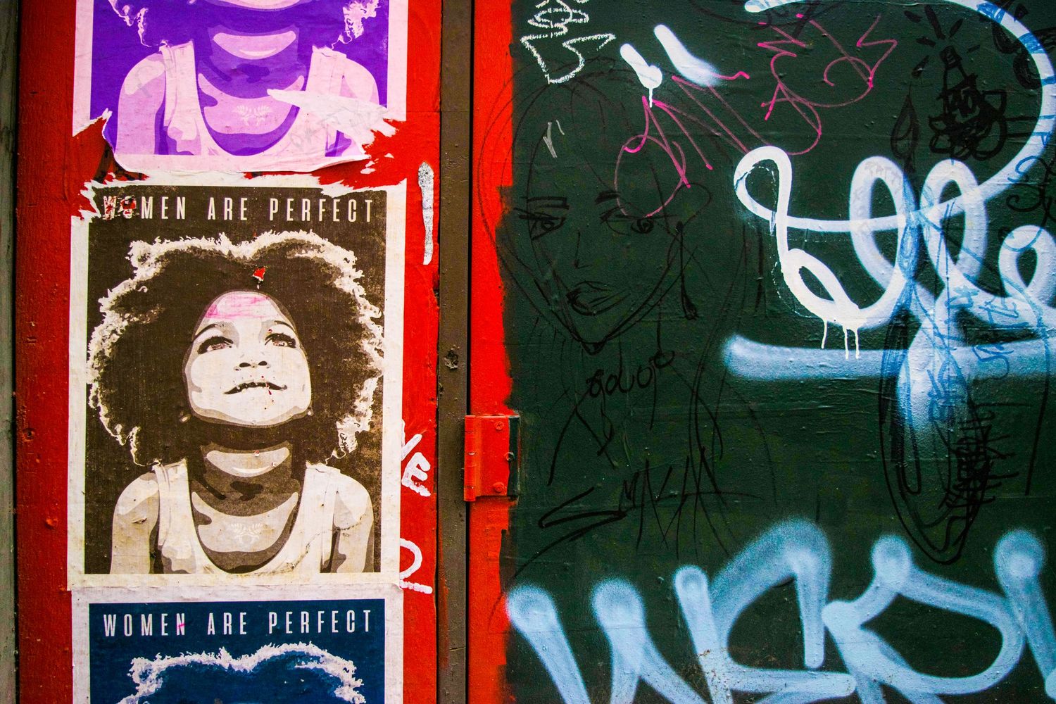Urban street art and posters on red wall with neon blue graffiti.