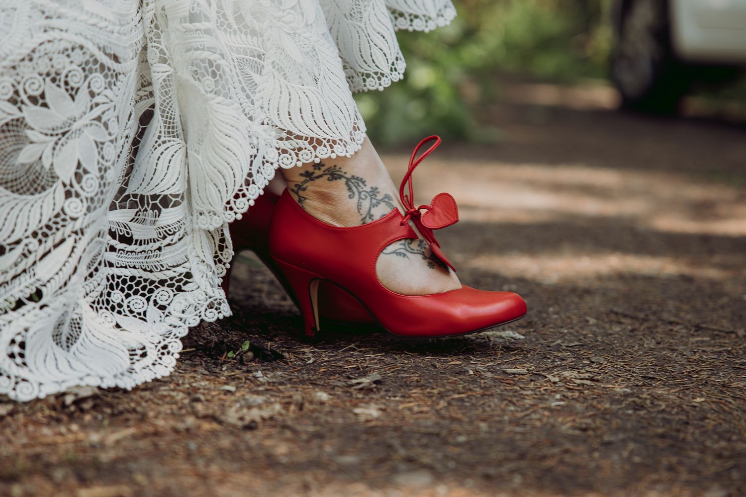 Close-up view of delicate white lace fabric and red shoes on a dirt path.
