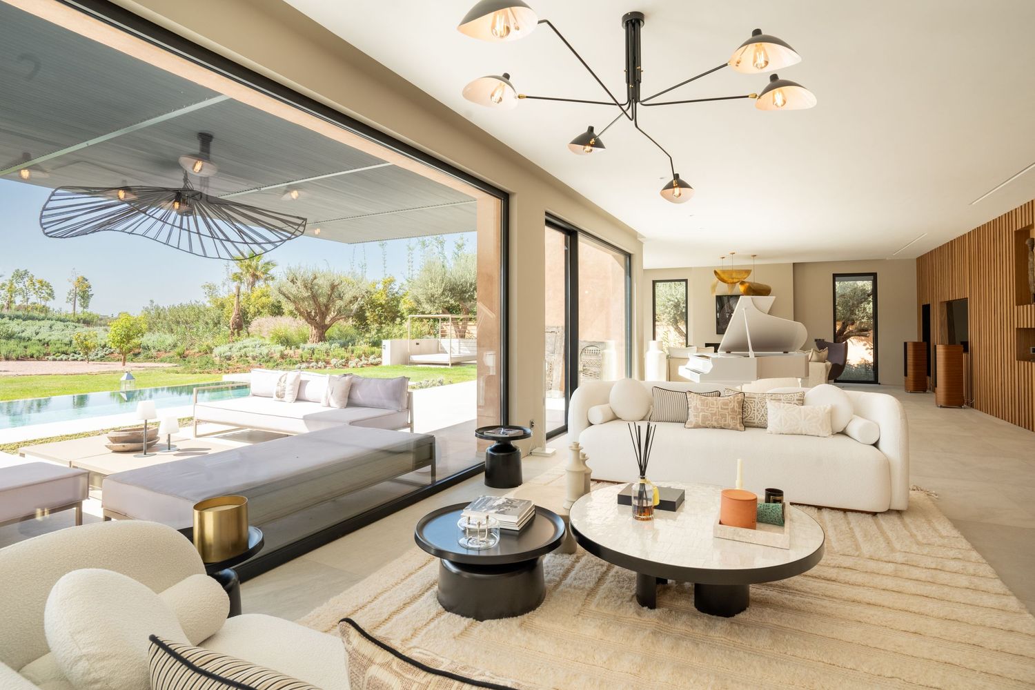 Luxurious living room with curved white furniture and pool view through large windows.