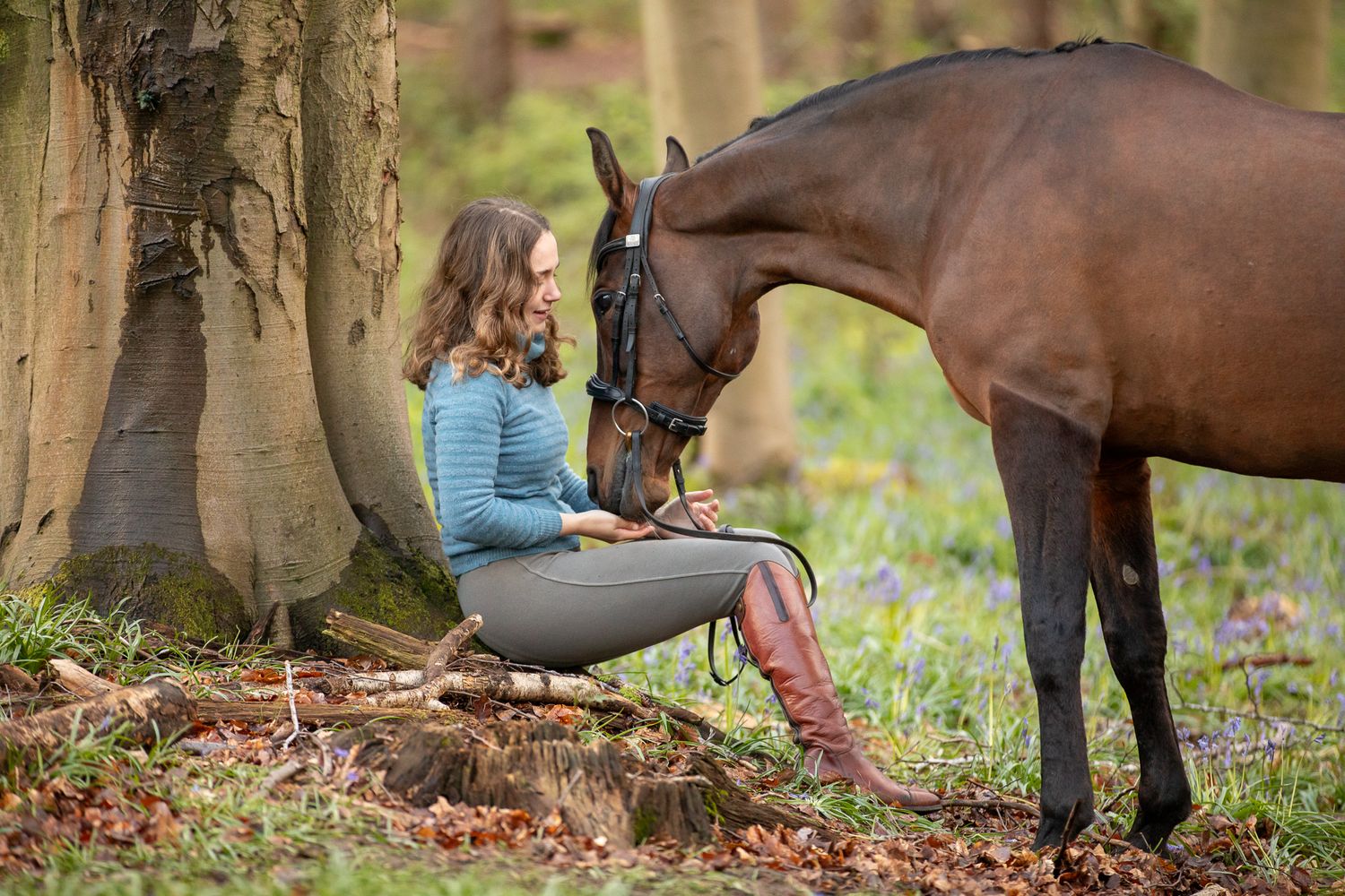 Horse and companion sharing a quiet moment while resting against a tree in a forest setting.