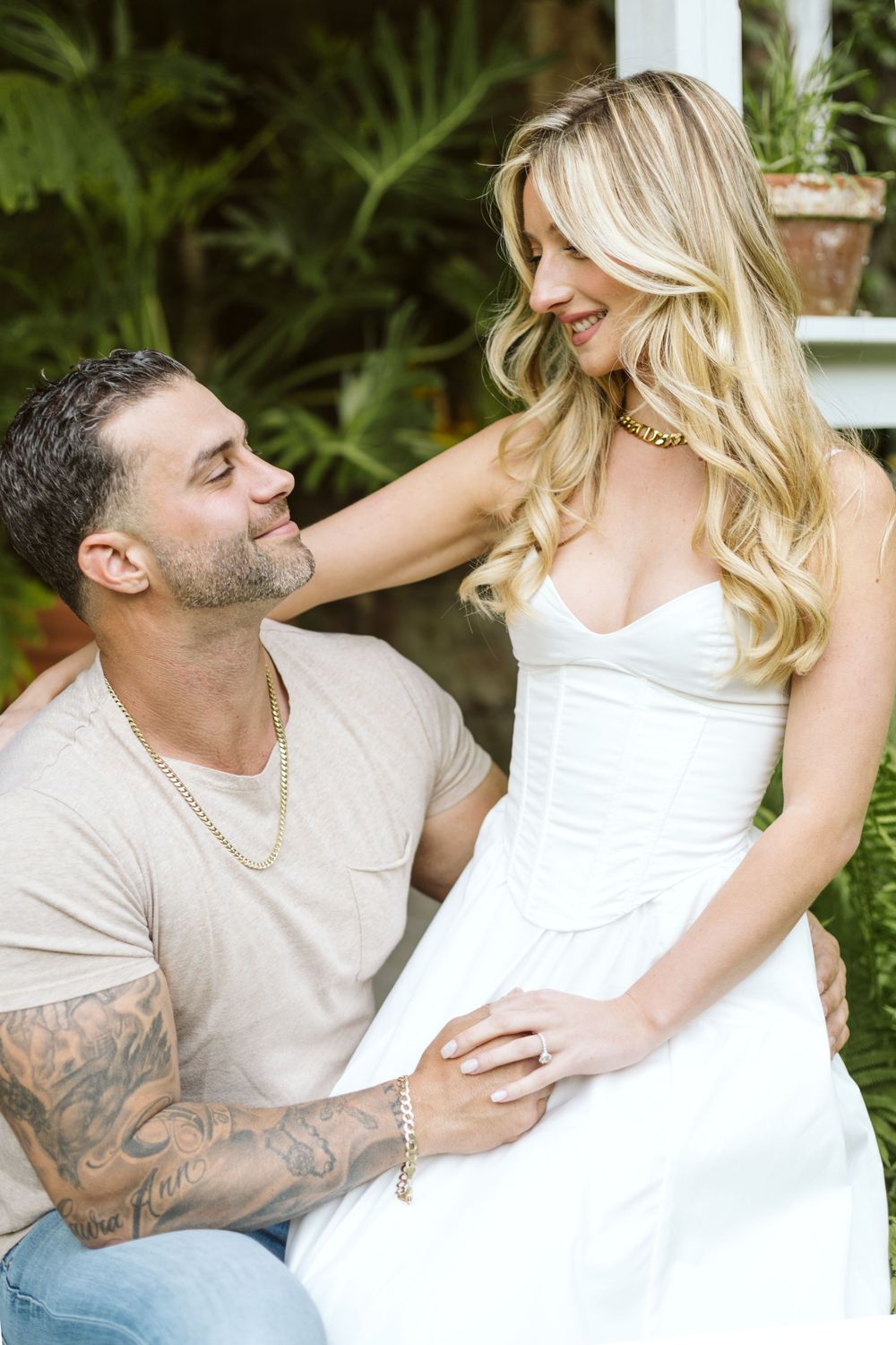 A romantic couple poses in a garden setting with a stone wall background.