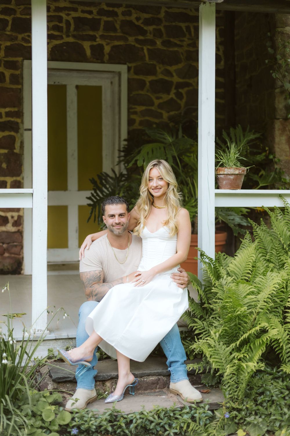 A couple sharing an intimate moment on stone steps surrounded by ferns and plants.