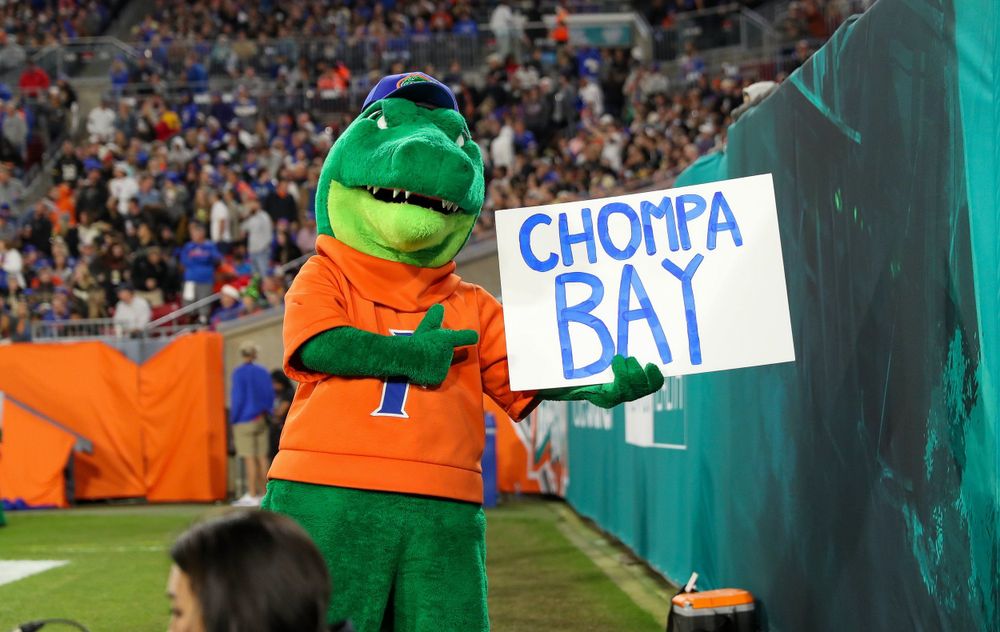 Albert the Alligator mascot holds a 'Chompa Bat' sign at a Florida Gators baseball game.