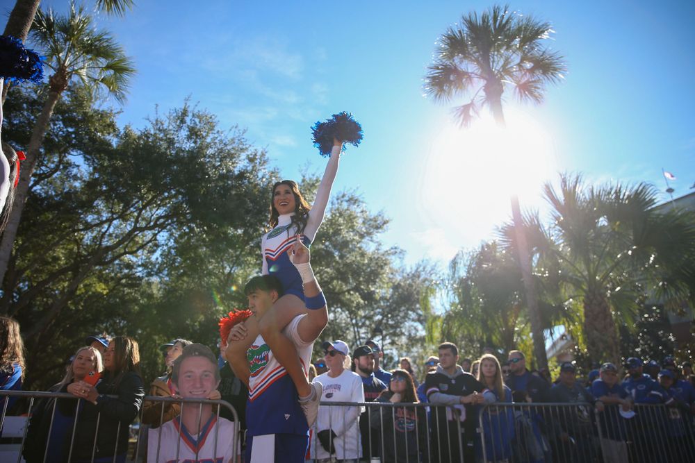 A cheerleader performs a high-flying stunt outdoors with palm trees in the background.