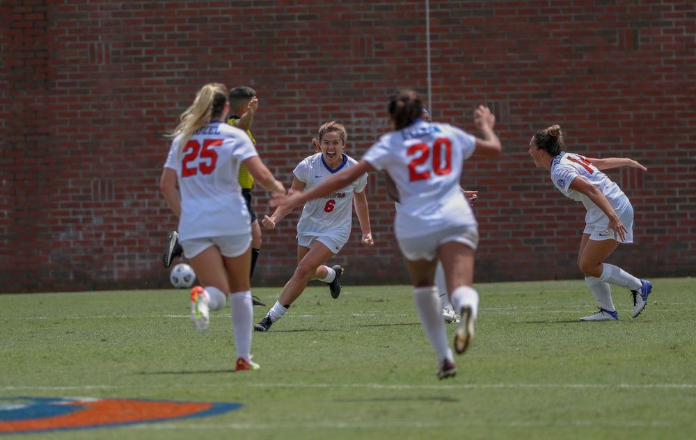 Soccer players compete for ball during intense match near brick wall.