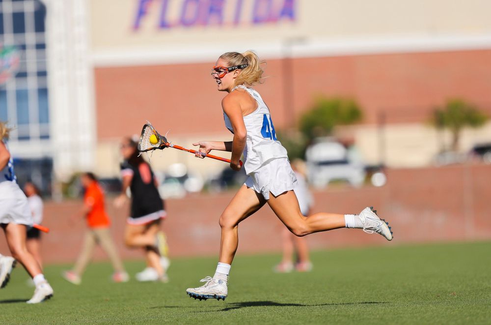 Lacrosse player sprints across field with stick during game.