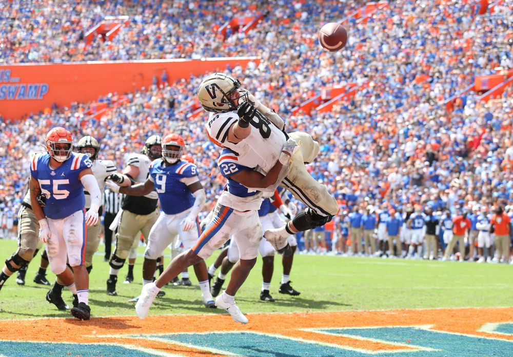 Football player leaping to catch a pass in the end zone during game action.