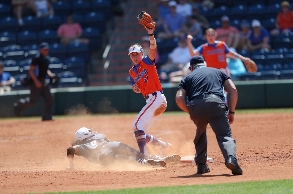 Baseball player slides into base as Florida Gators defender jumps to catch throw during game.
