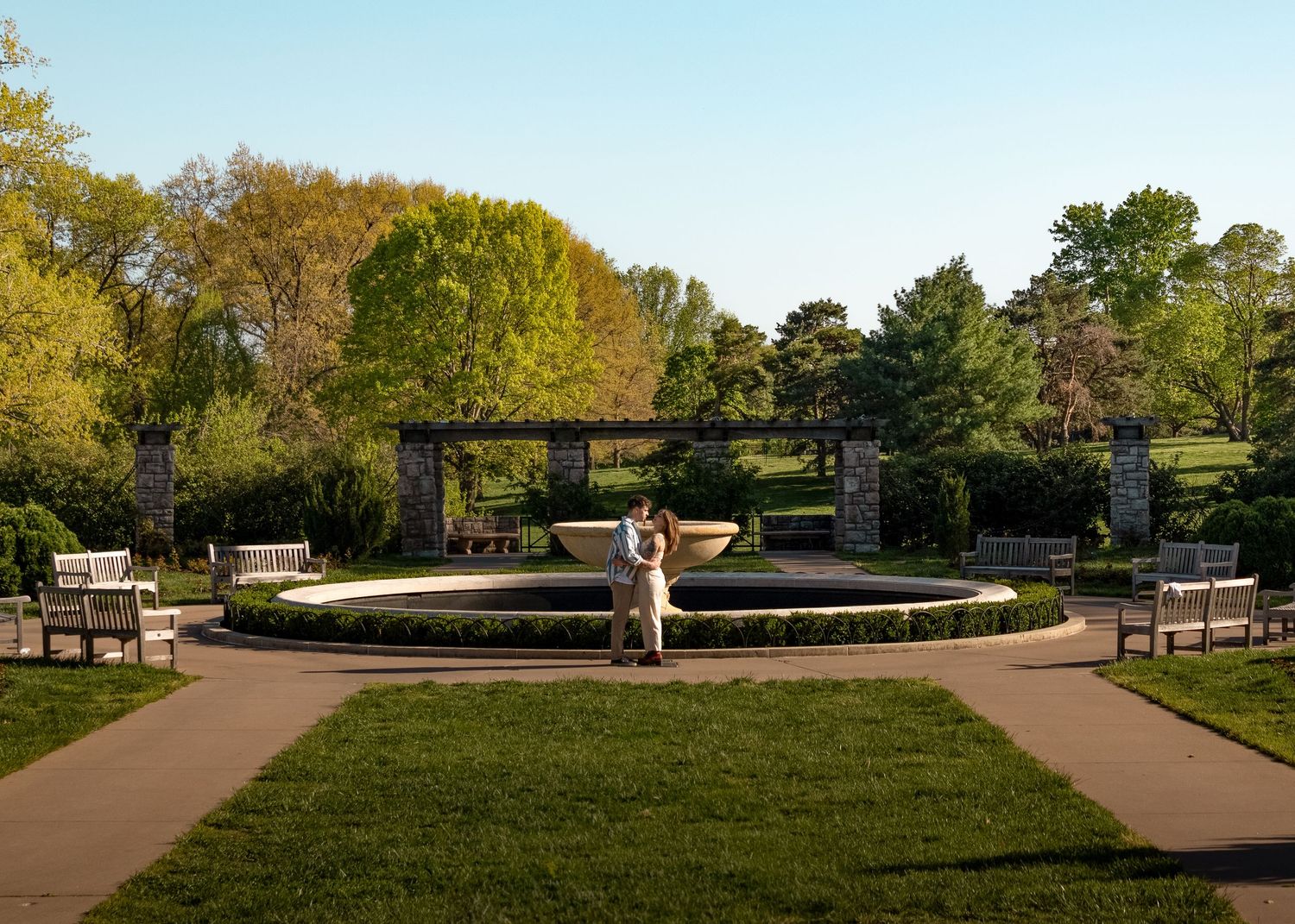 Couple embracing in front of fountain inside of a rose garden