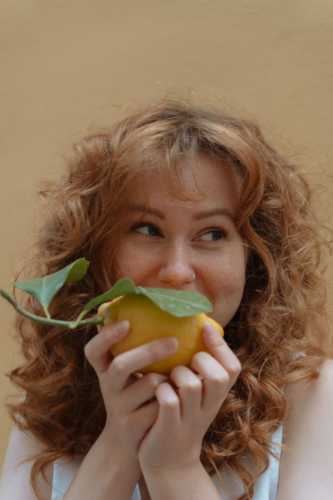 A playful portrait showing someone holding a fresh yellow apple with green leaves.