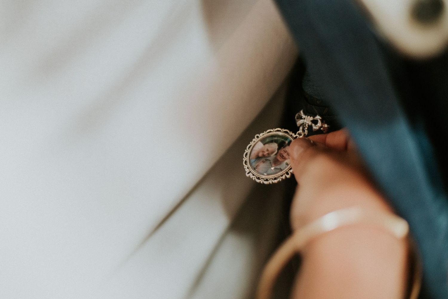 Close-up of a delicate silver locket charm pinned to teal wedding attire with ribbon.