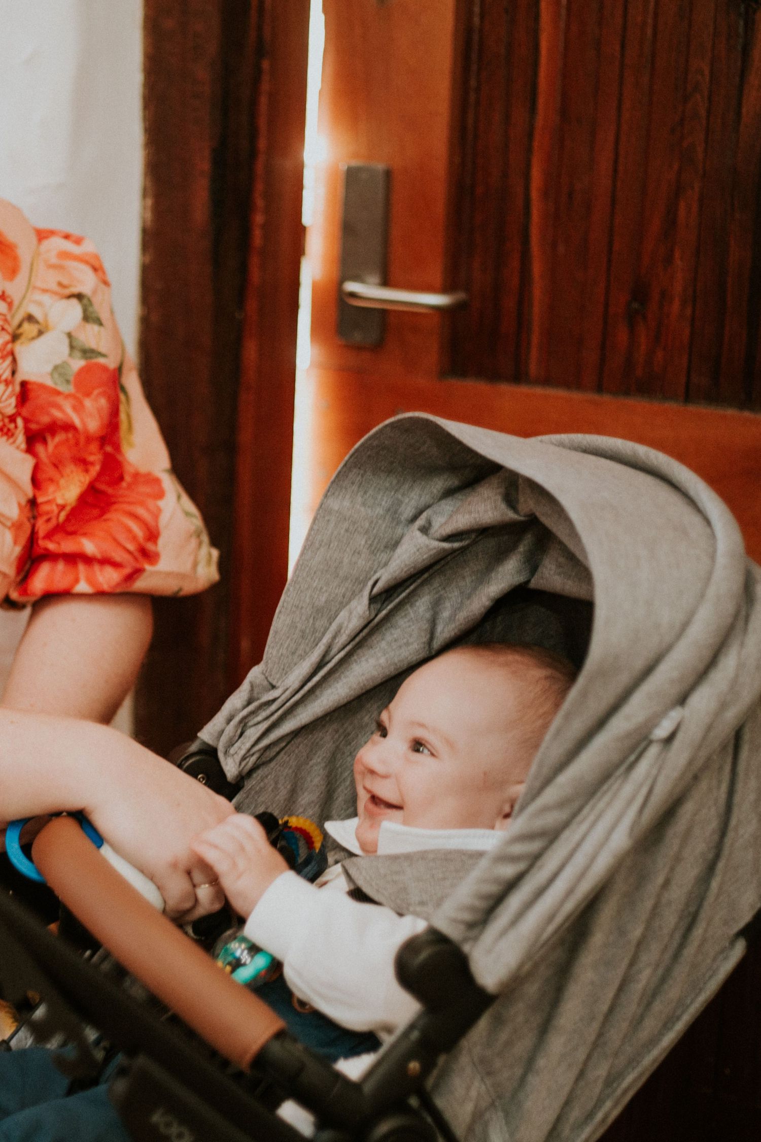 Happy smiling baby in a grey pram at a wedding venue doorway with floral dress nearby.