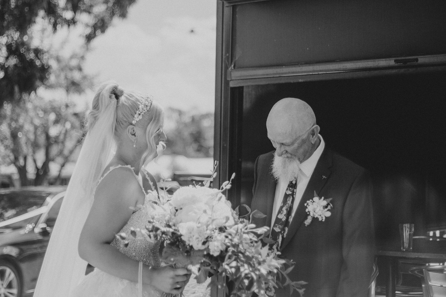 Black and white photo of bride and older man sharing tender moment outside wedding venue door.