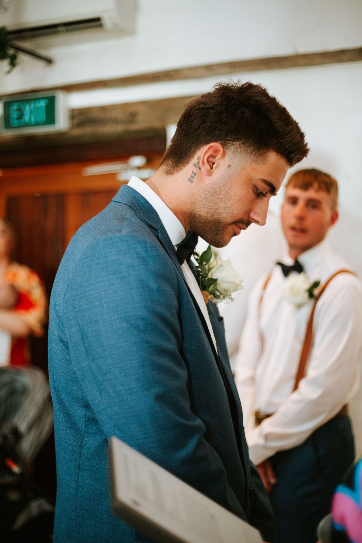 Emotional groom in blue suit with bow tie and boutonniere looks down during wedding ceremony.