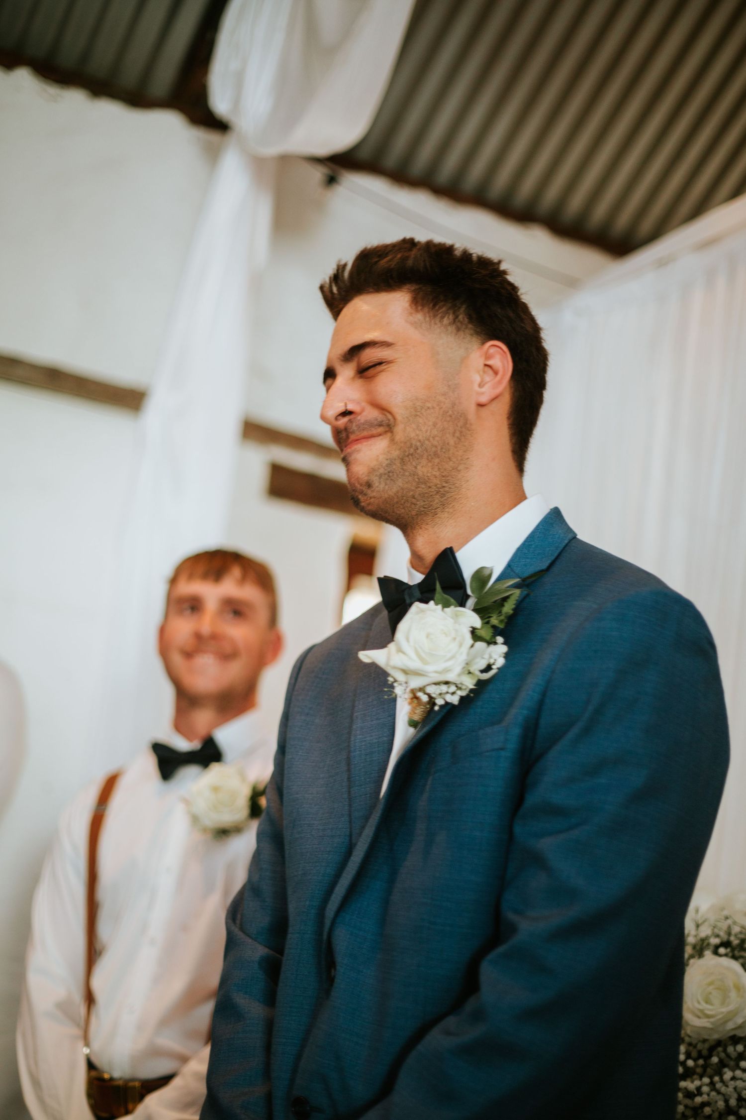 Emotional groom in blue suit closing eyes with smile at wedding ceremony altar.