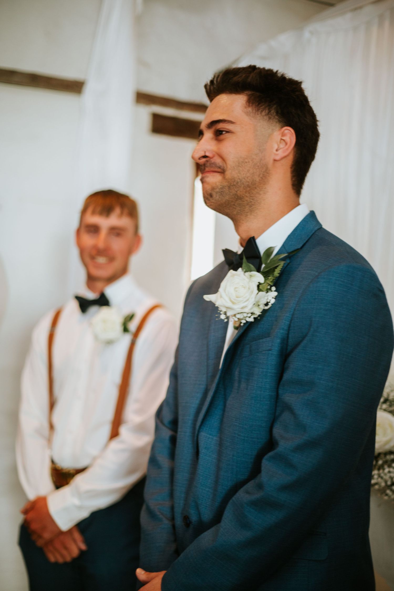 Groom in blue suit with white rose boutonniere standing at wedding ceremony altar.
