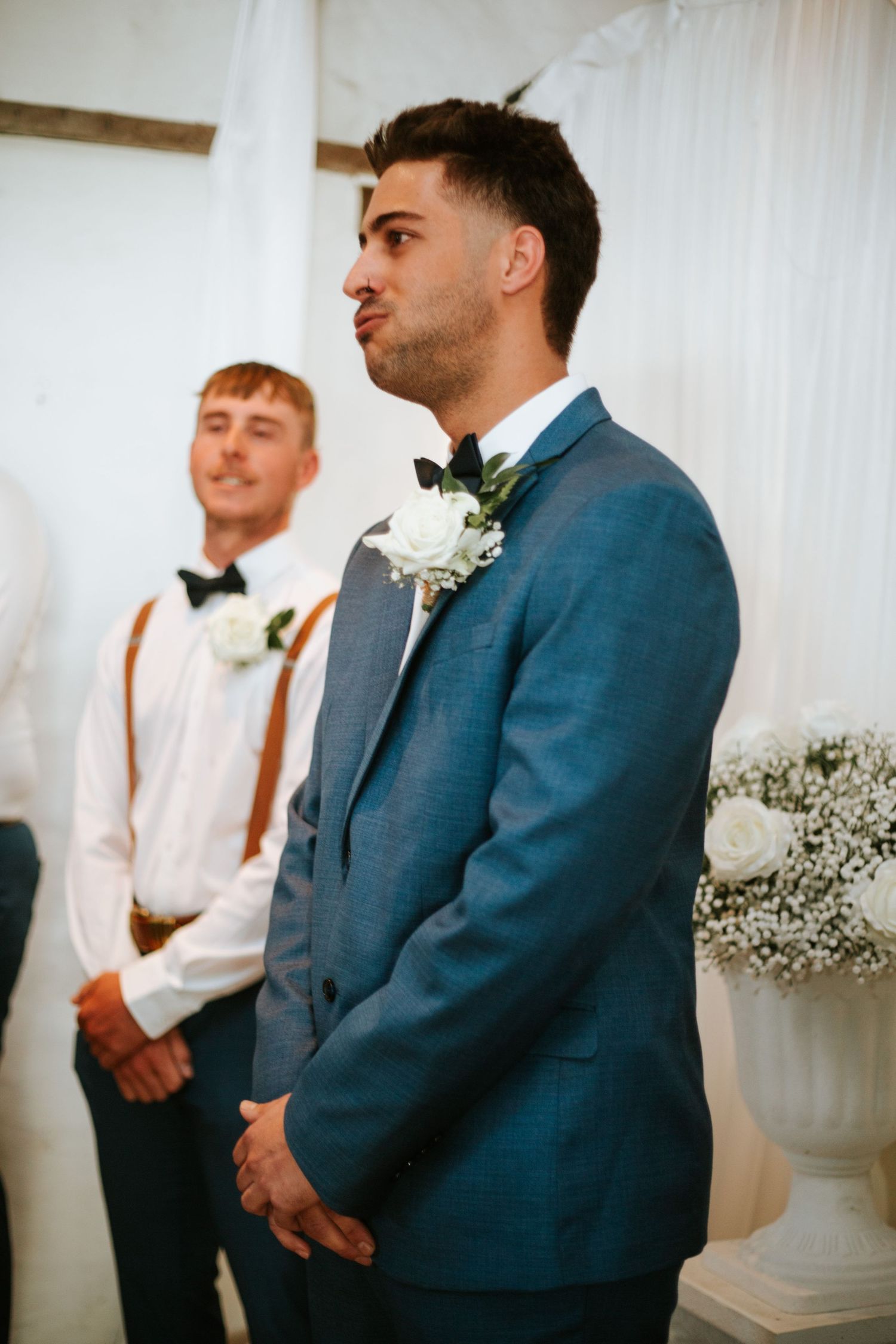 Groom in blue suit exhaling nervously at wedding altar with smiling groomsman behind.